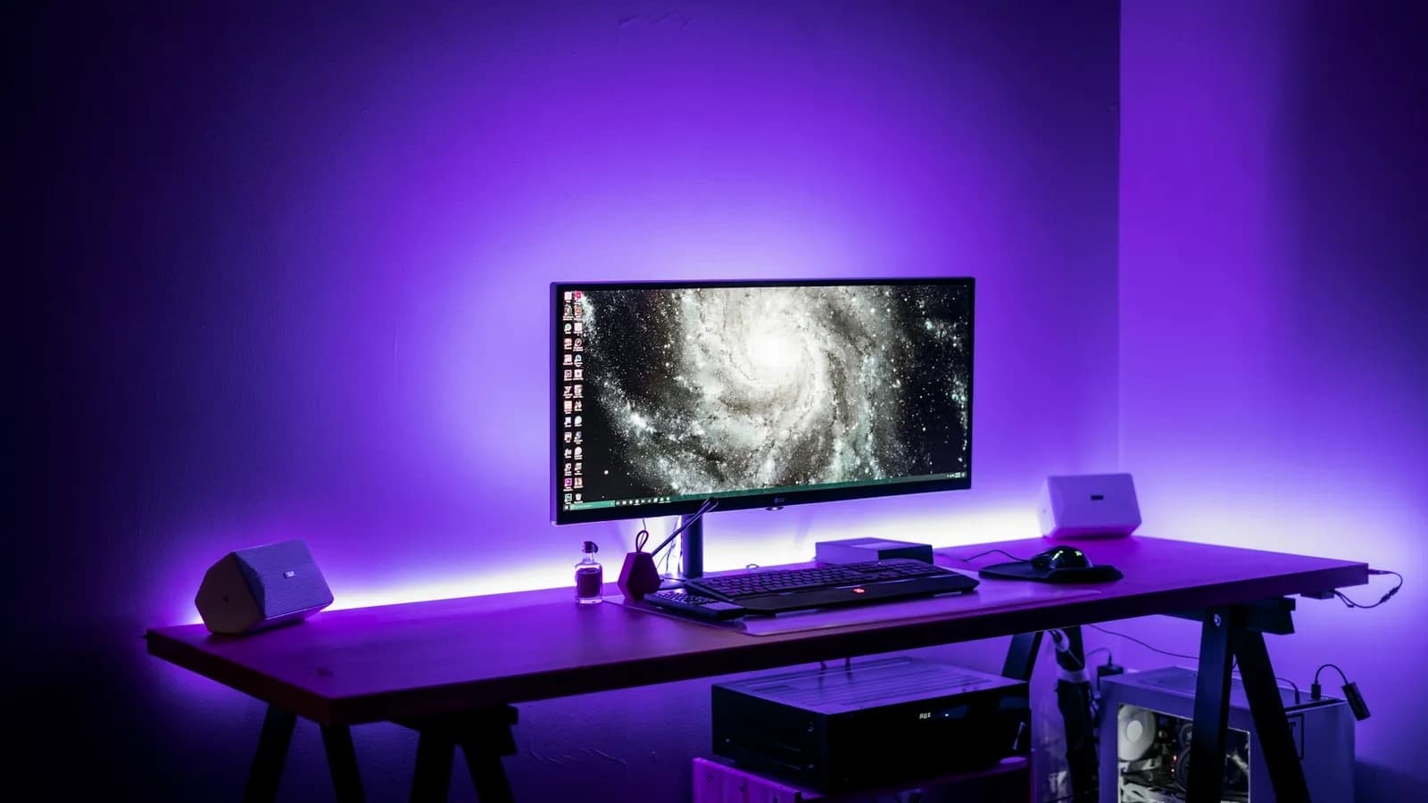 A desk with an ultrawide monitor and a keyboard lit by purple LED light