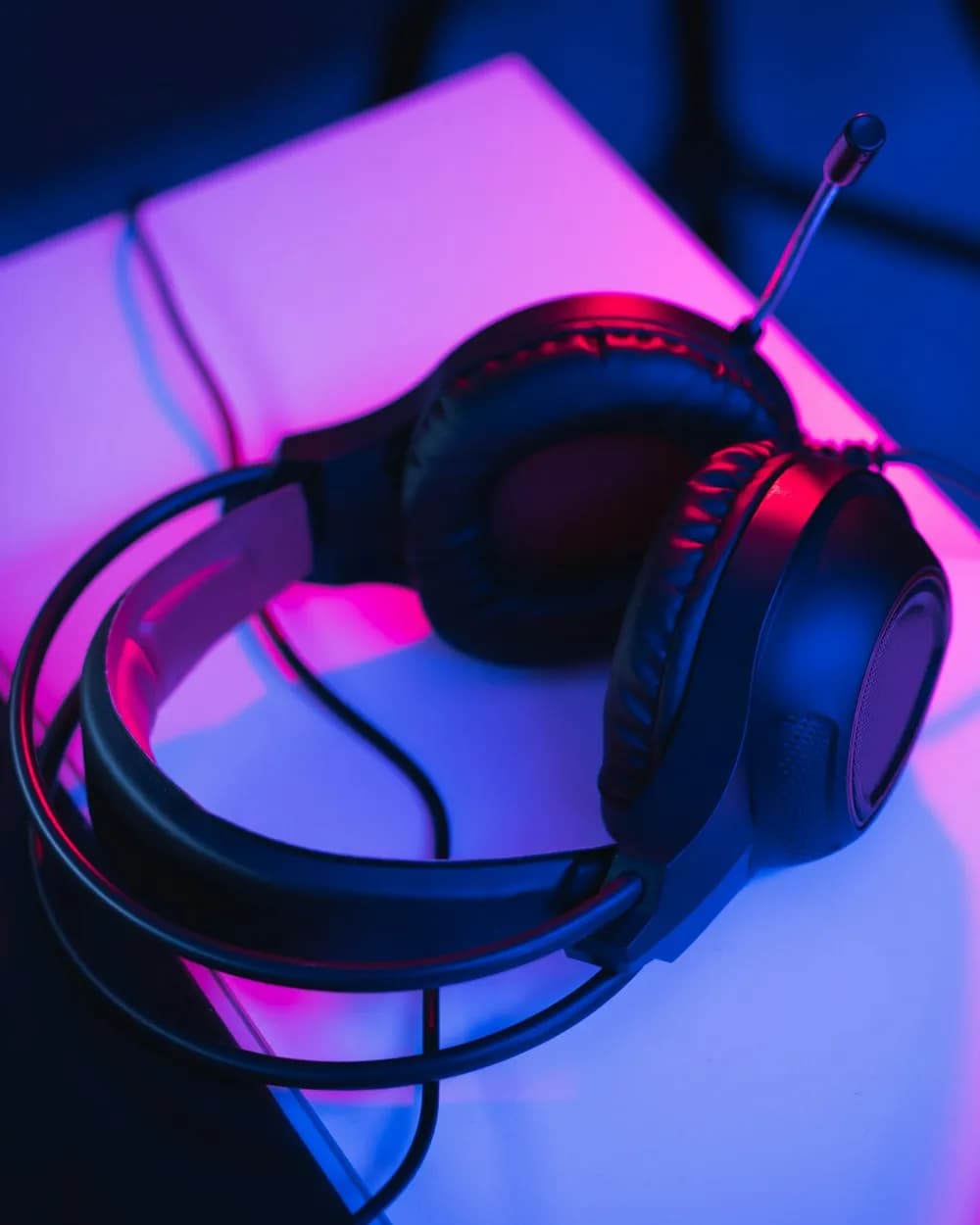 An over-ear gaming headset on a desk under pink and blue light