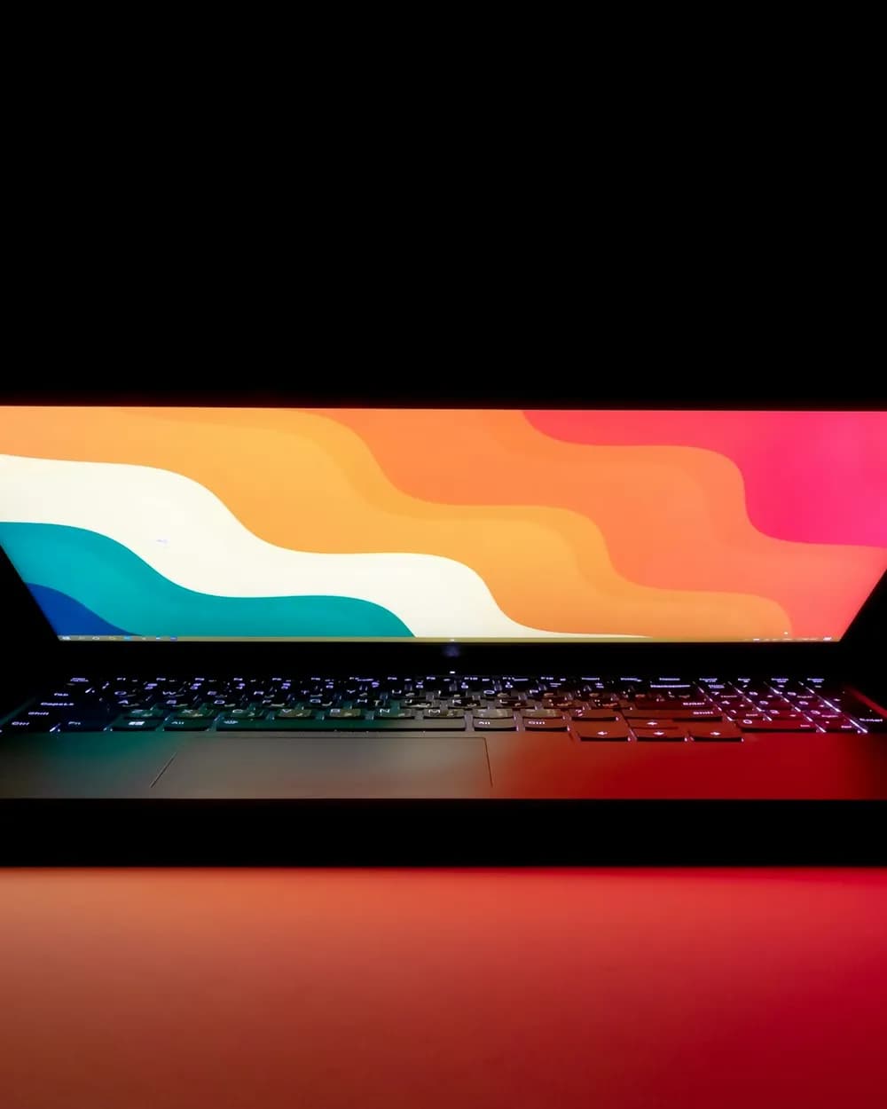A thin laptop with a colourful screen in a dark room
