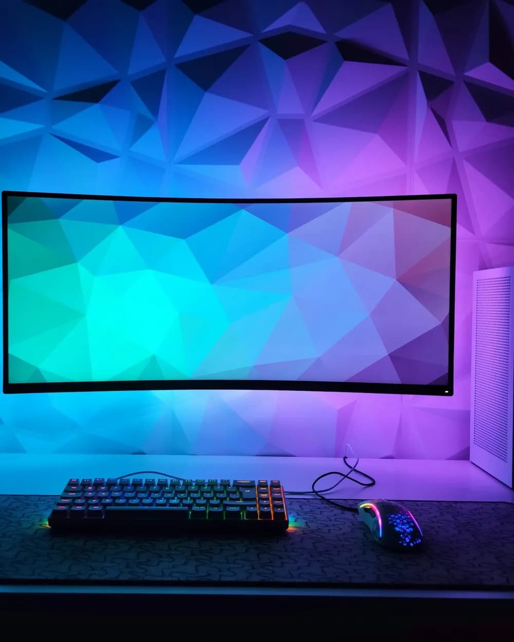 A curved ultrawide monitor on a desk lit in blue and purple